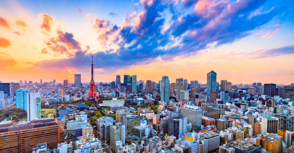 A vibrant cityscape of Tokyo at sunset, with colorful clouds in the sky, skyscrapers, and the iconic red Tokyo Tower visible among the buildings.